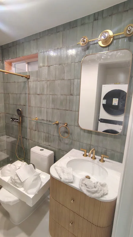 Glossy green tile pairs with a rounded wood vanity and brass lighting.