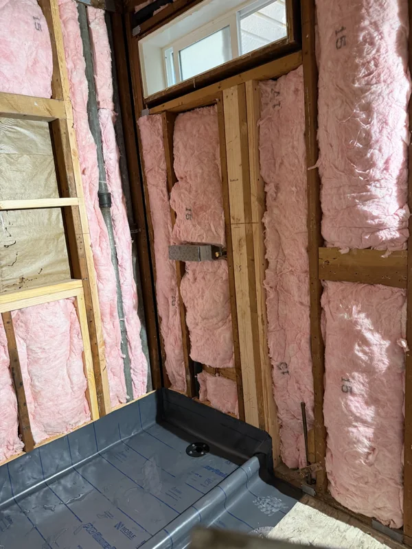 Exposed framing and insulation around the shower base and window.